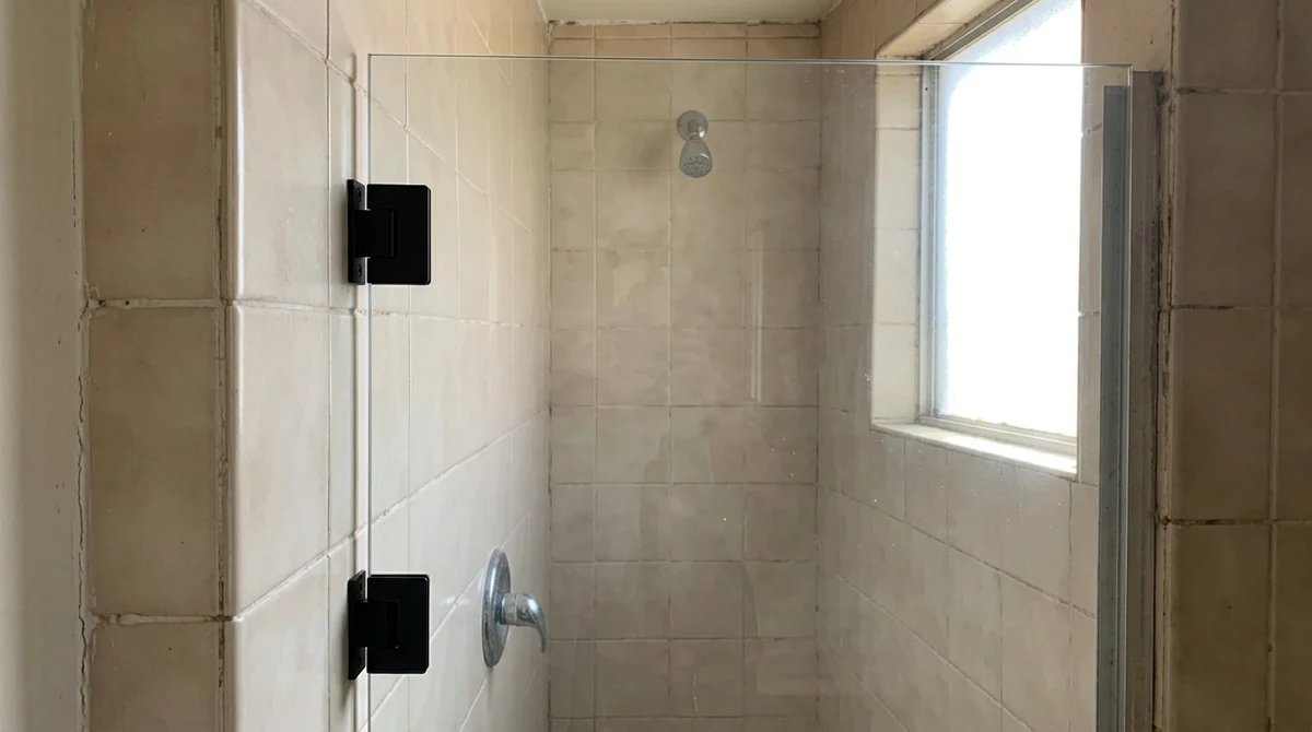 After: The same shower with a new heavy glass pivot door hanging perfectly straight on matte black pivot hinges, no gaps, same tile and lighting