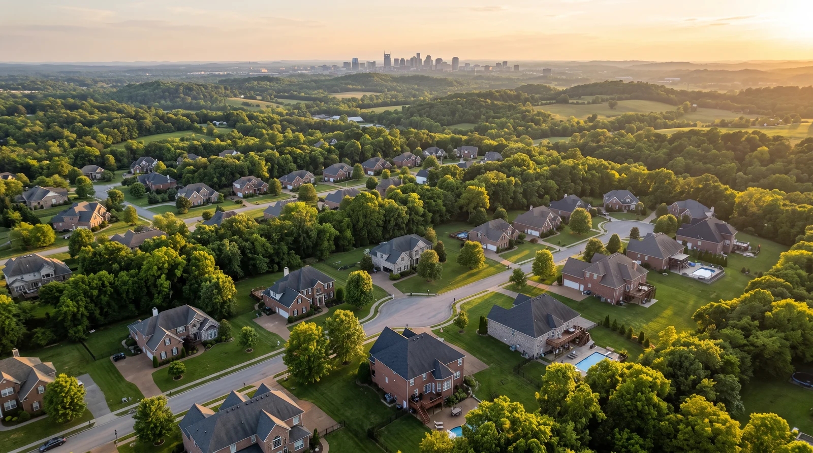 Aerial View of Middle Tennessee Neighborhoods and Homes | Music City Shower Doors An aerial view over a green Middle Tennessee neighborhood at golden hour showing brick and stone homes, mature trees, rolling hills in the distance and a glimpse of the Nashville skyline far away