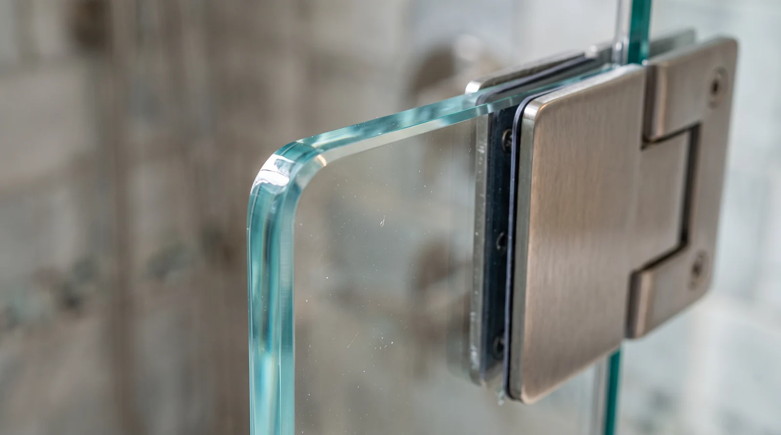 A macro close-up of the polished edge and corner of thick clear tempered glass beside a stainless steel hinge in a shower, sharp reflections and subtle light refraction, shallow depth of field