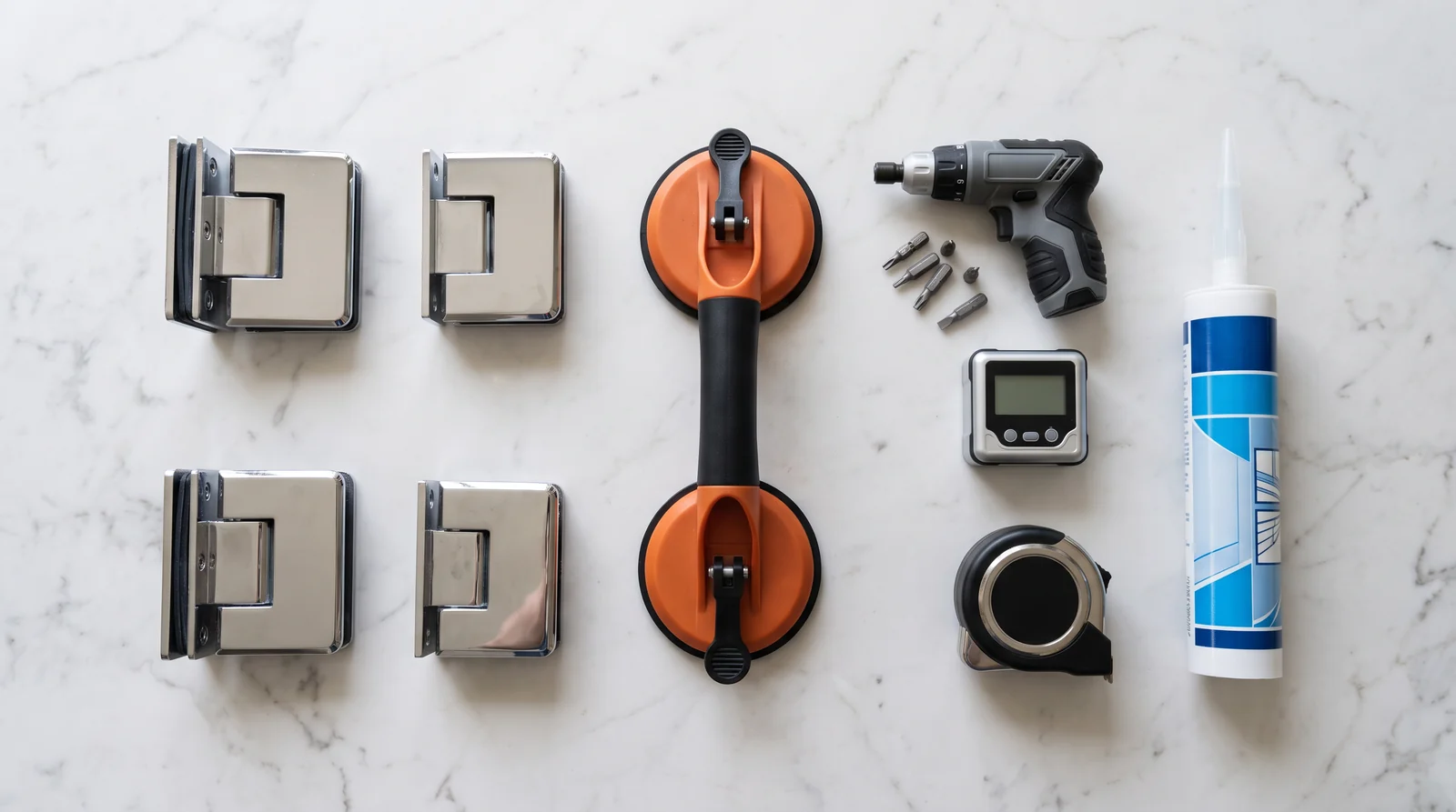 A neat flat-lay on a white marble countertop of glass shower door hinges, clamps, a suction-cup glass lifter, a torque driver, a digital level, a tape measure and a tube of clear silicone, soft overhead light, shallow depth of field