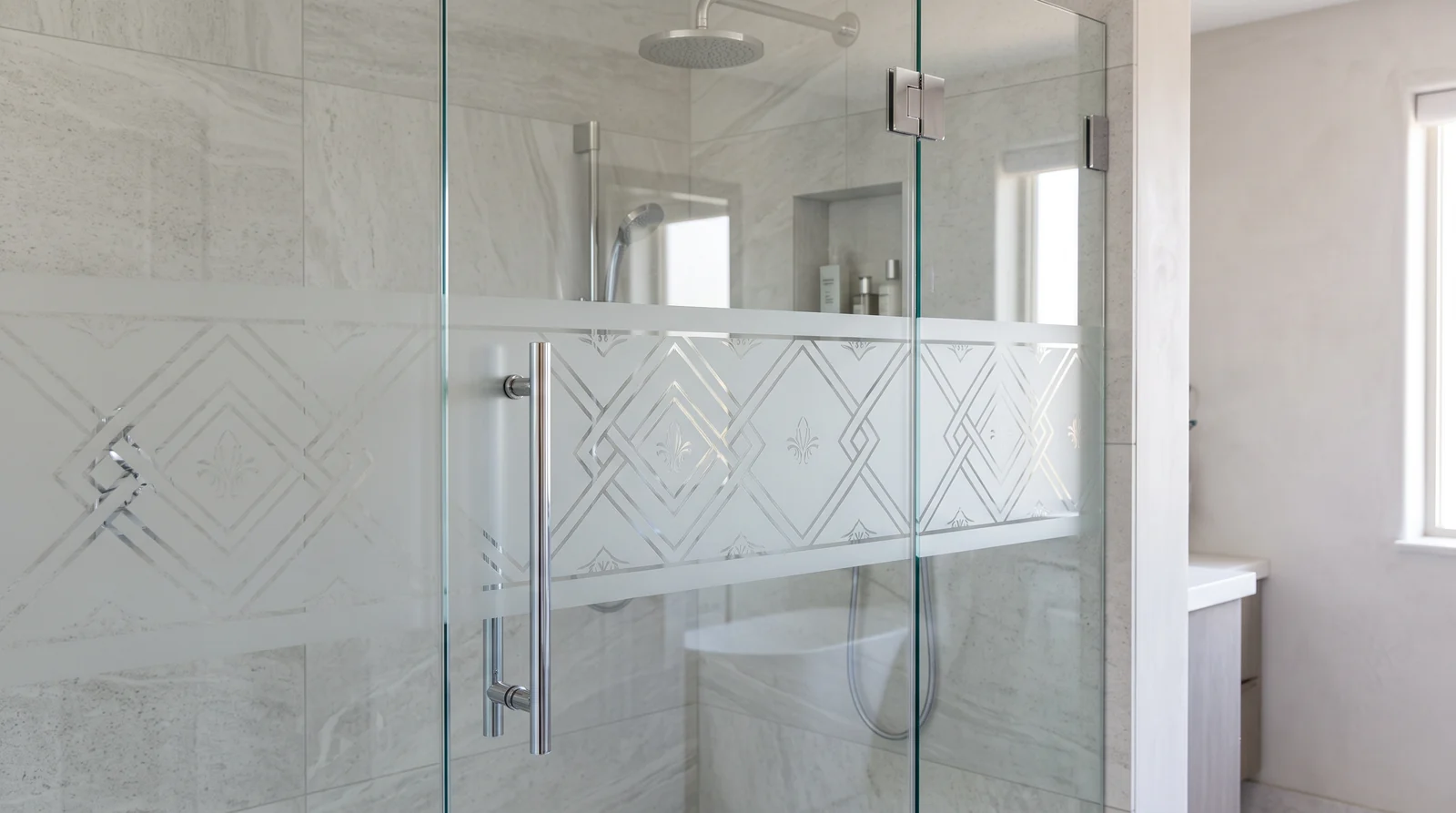 A glass shower door with an elegant etched geometric pattern in a frosted band, soft light, tile walls and chrome hardware, calm luxury bathroom
