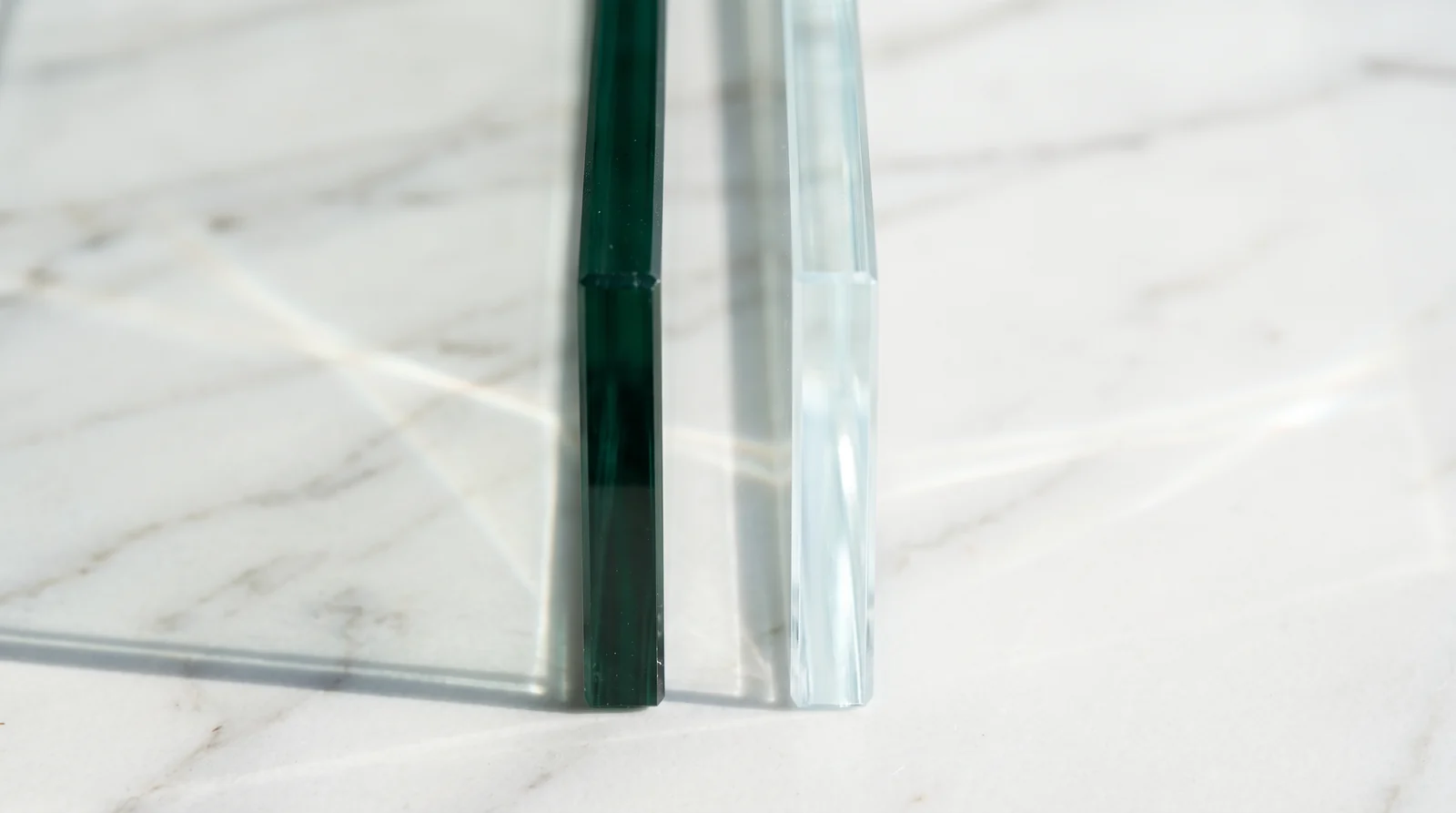 A side-by-side look at ultra-clear low-iron glass and standard clear glass edges showing the green tint of standard glass, in front of white marble tile, bright natural light
